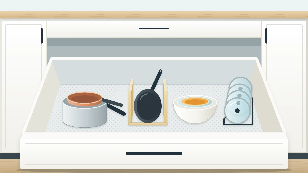A deep lower drawer pulled fully open with nested saucepans, a frying pan on edge in a divider, lids in a side rack and nested mixing bowls