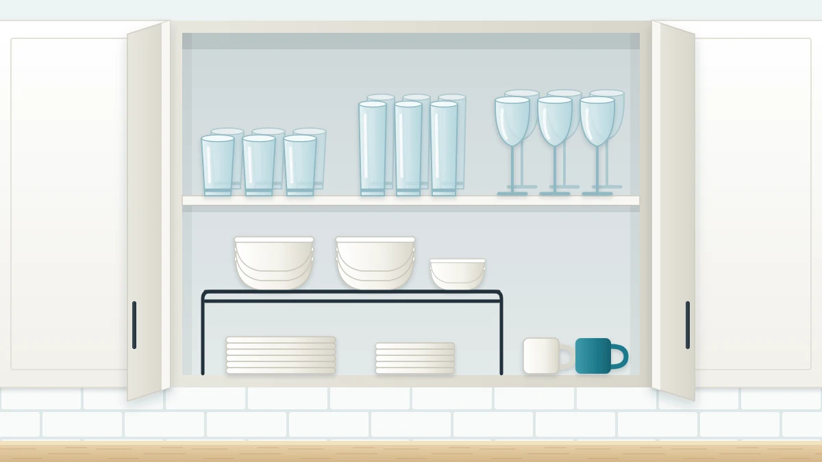 An open upper cabinet with dinner and side plates in two short stacks, bowls on a wire shelf riser and three neat rows of drinking glasses above