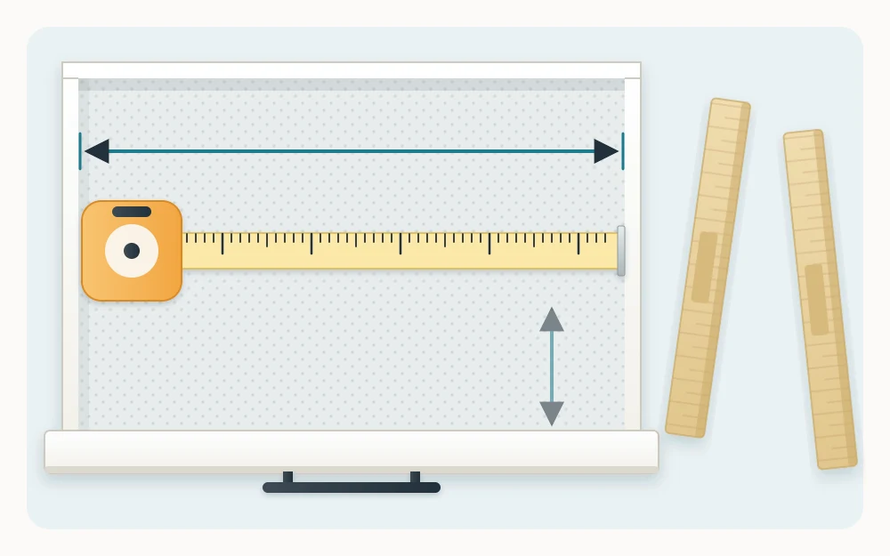 An empty open drawer seen from above with a tape measure laid across its inside width and two loose bamboo divider strips beside it