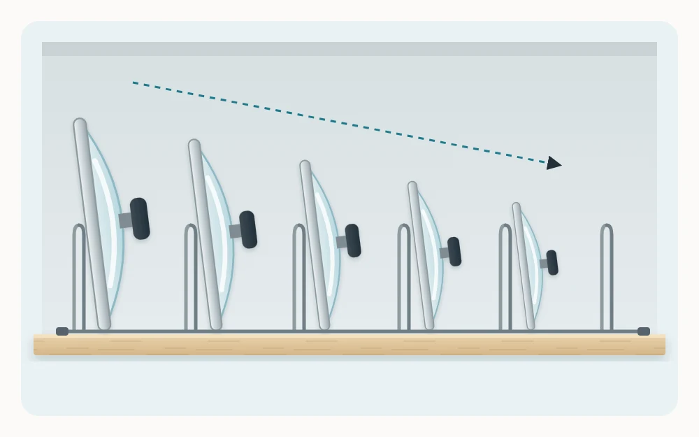Five pot lids of graduated sizes standing on edge in an upright wire file-style rack on a wooden shelf, seen from the side